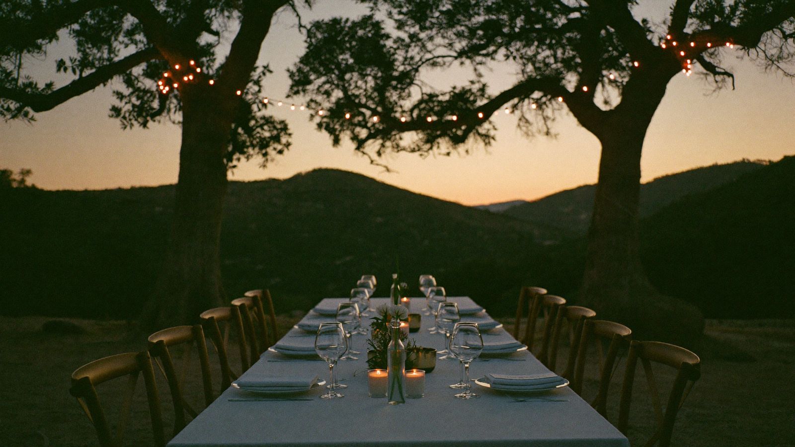 Mesa de gala preparada al aire libre bajo las encinas de la dehesa al anochecer